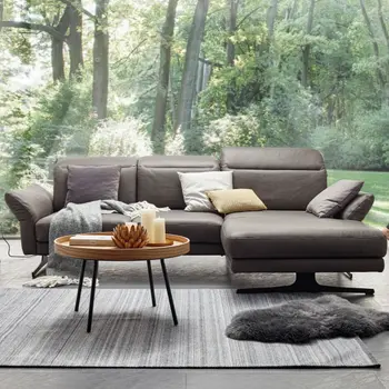 Ecksofa in grauem Leder vor einer großen Fensterfront mit Blick ins grüne.