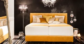 Goldenes Boxspringbett mit Kristallleuchter und Kissen.