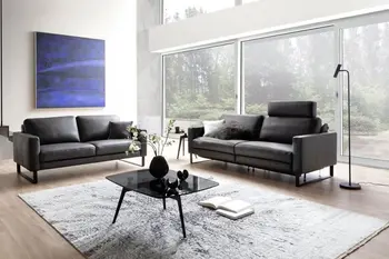 Zwei braune Ledersofas, die im rechten Winkel zueinander stehen, bei dem einen ist eine Kopfstütze hochgeklappt.