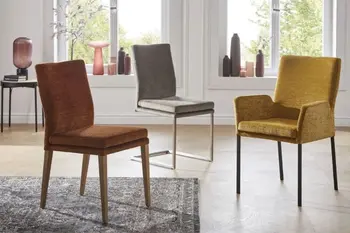 Orangener Esszimmerstuhl mit Holzgestell neben einem grauen Freischwinger Stuhl mit silbernem Gestell und einem gelben Armlehnstuhl mit schwarzen Beinen. 