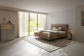 Beiges Design Polsterbett mit hohem gestepptem Kopfteil in einem gemütlichen Raum mit bodentiefen Fenstern.