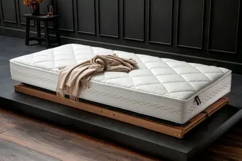 Hochwertige Matratze mit Rautensteppung, die auf einem Lattenrost auf dem Boden liegt, auf der Matratze liegt eine beige Wolldecke.