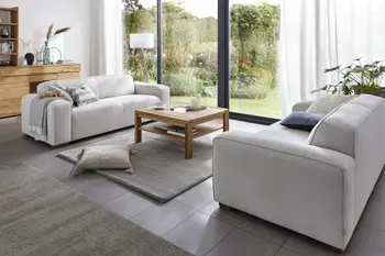 Zwei graue Sofas mit runden Ecken die sich gegenüber stehen und mit Kissen und einer Decke dekoriert sind.