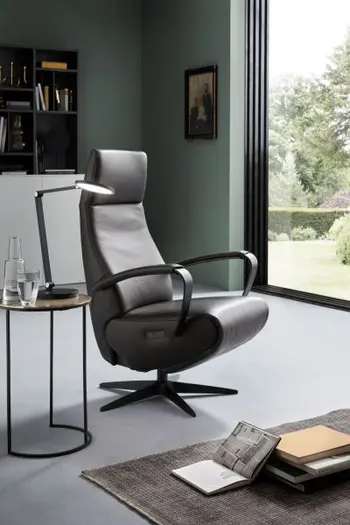 Relaxsessel mit schwarzem Lederbezug und offenen schwarzen Armlehnen in einem hellen modernen Zimmer mit rundem Beistelltisch.