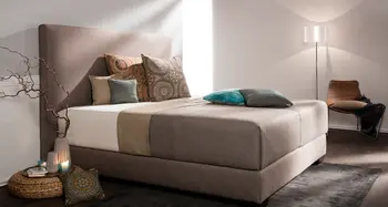 Modernes Polsterbett mit bunten Kissen und Stehlampe.