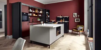 Inselkueche mit weisser Kuecheninsel und rot-schwarzer Kuechenzeile in Lackoptik vor roter Wand.