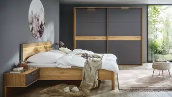 Massivholzbett mit Nachtkonsolen mit grauen Elementen sowie einem großen Schwebetürenschrank mit grauen und Holzelementen an den Türen.