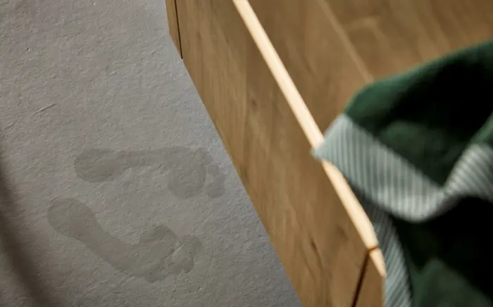 Zwei nasse Fußabdrücke auf einem rauen Steinfußboden vor einem Badezimmerschrank